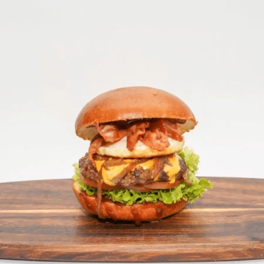 US Burger mit Cheddar, Ei, Bacon und BBQ-Soße auf einem Holzbrett