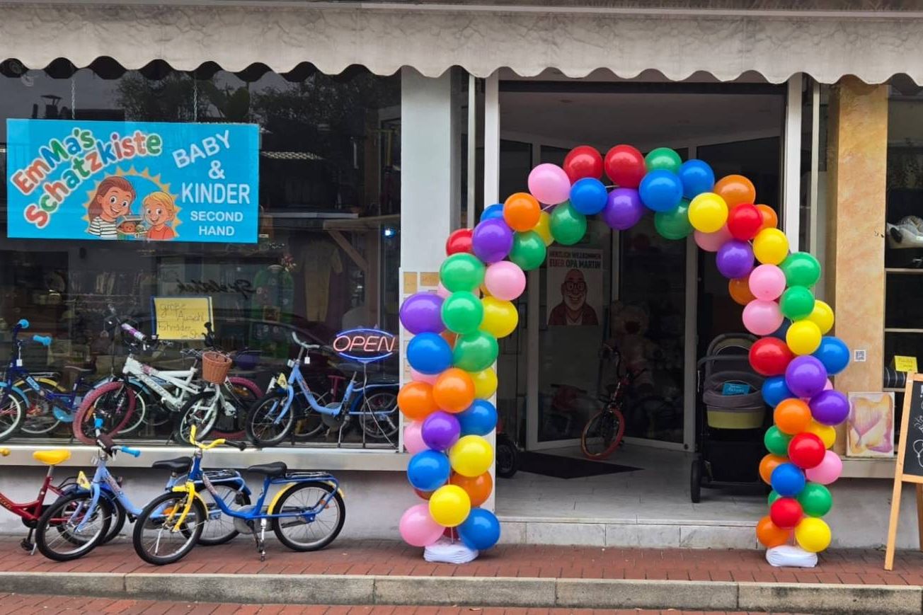 Schaufenster von Emma's Schatzkiste mit bunten Kinderrädern, Luftballonbogen am Eingang und dem Laden-Schild